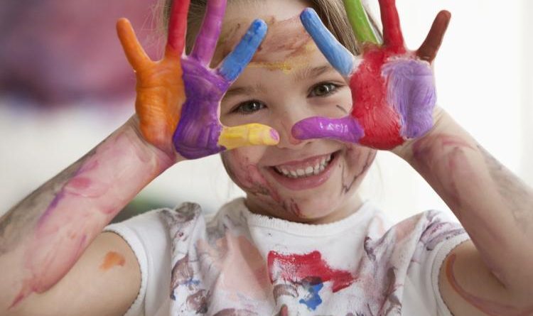 Una bambina sorridente mostra le mani dipinte di tanti colori